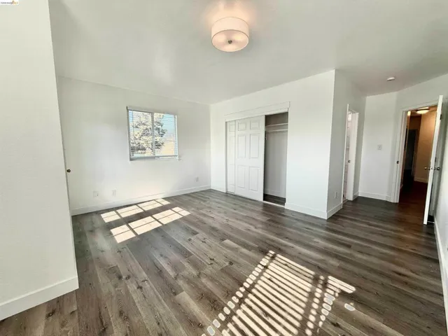Spacious room featuring wood-finish flooring, white walls, and a multi-pane window with blinds