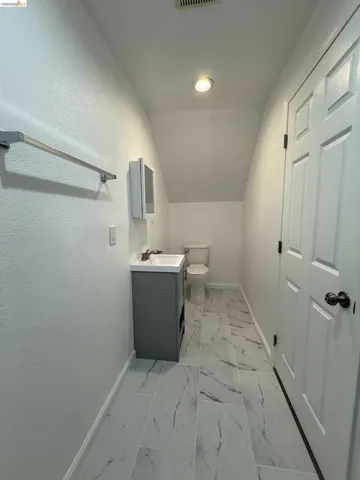 Bathroom featuring a white toilet, a gray vanity with a built-in sink, a wall-mounted medicine cabinet, recessed lighting, and white marble-look tile flooring