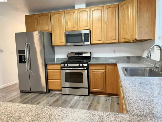 Kitchen featuring light wood cabinetry, stainless steel appliances, granite-look countertops, and wood-finish flooring