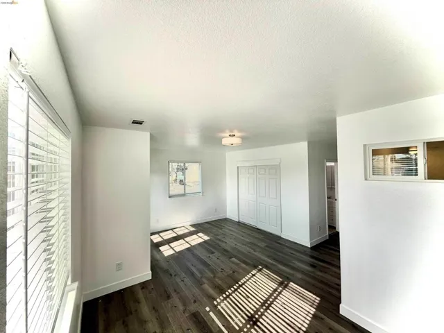 Spacious room with dark wood-finish flooring, white walls, and bright overhead lighting