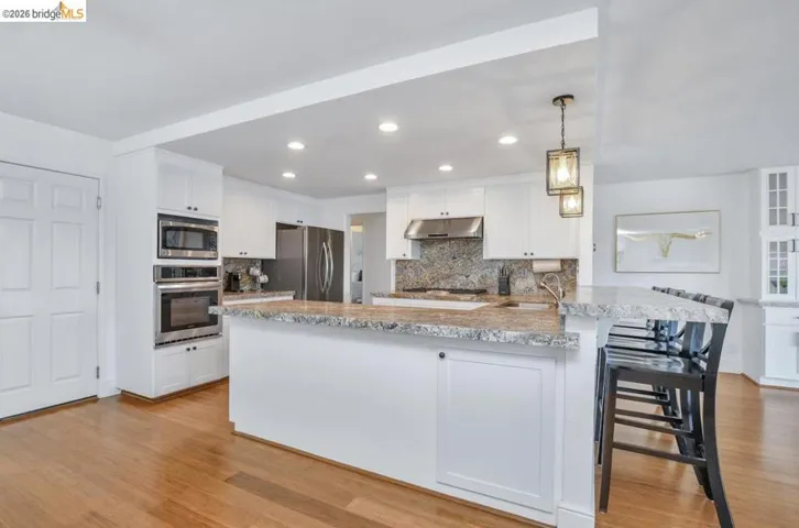 Kitchen featuring white cabinetry, wood-finish flooring, stainless steel appliances including a built-in microwave and oven, and recessed lighting