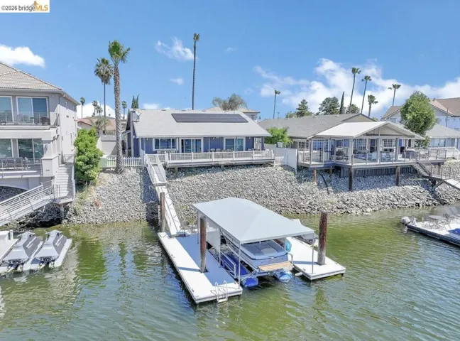 Waterfront residence featuring a private boat dock with a covered slip, an elevated deck, and solar panels on the roof