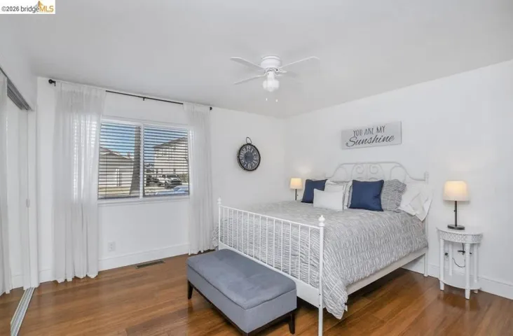 Bright bedroom featuring wood-finish flooring, a ceiling fan, window with blinds, and white walls