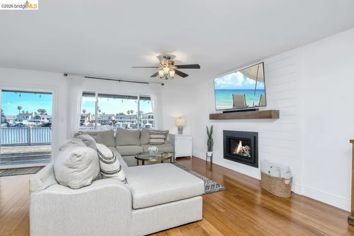 Spacious living area featuring wood-finish flooring, a ceiling fan, and large windows