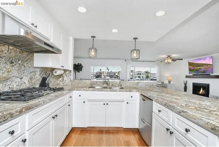 White shaker cabinetry and light-toned countertops define this kitchen, featuring a stainless steel range hood, built-in gas stovetop, and an undermount sink