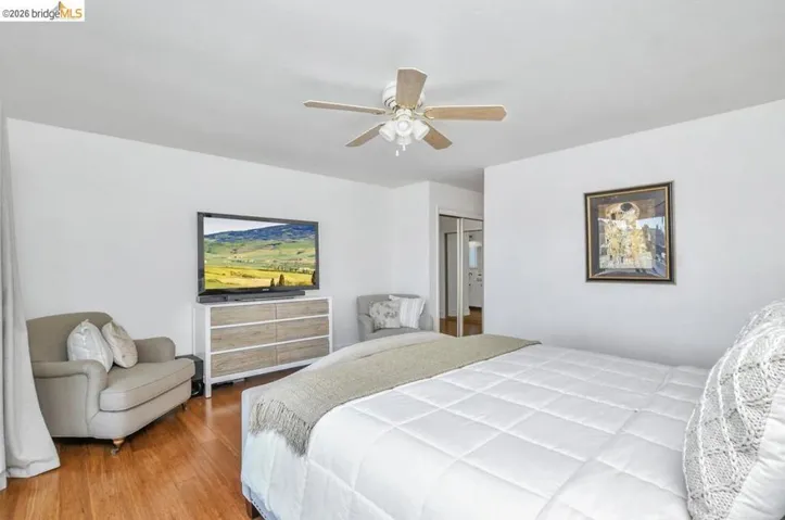 Bright bedroom featuring wood-finish flooring, a ceiling fan with integrated lighting, and white walls