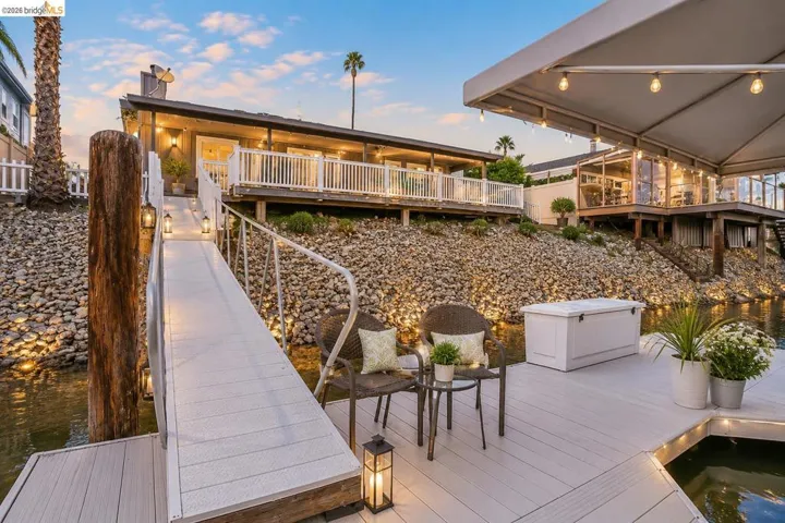 Waterfront property featuring an elevated deck, private dock, and a covered patio area with string lighting