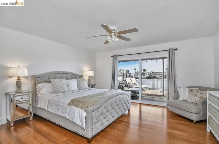 Hardwood flooring and white walls define this bedroom, featuring sliding glass doors opening to a waterfront deck