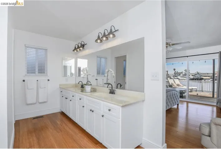Double vanity with stone countertop, wood-finish flooring, and natural light from a window with blinds