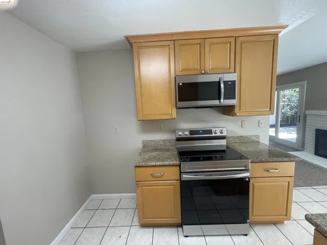 Kitchen area featuring light wood cabinetry, stainless steel microwave, and a glass-top electric range