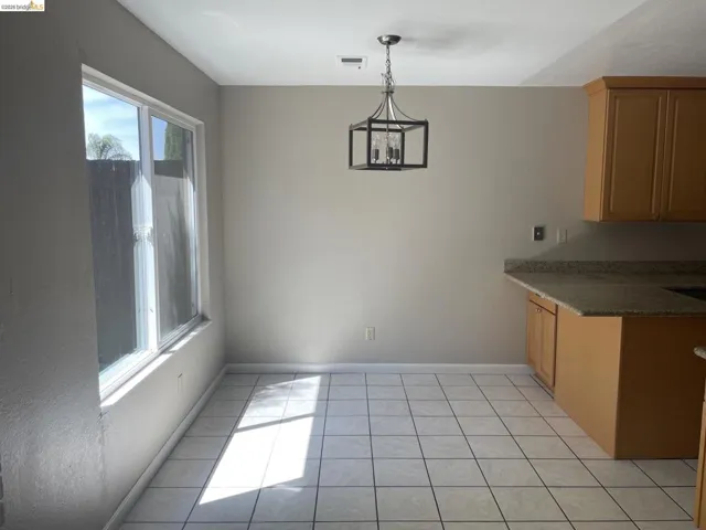 Dining area featuring a modern geometric chandelier, large sliding window, light-toned walls, and ceramic tile flooring