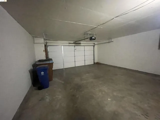 Attached garage featuring a white sectional overhead door, automatic garage door opener, concrete flooring, and painted walls