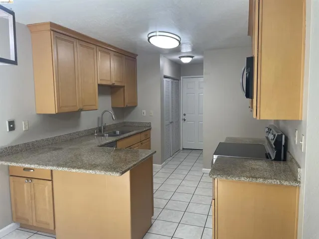 Kitchen featuring light wood cabinetry, granite-finish countertops, stainless steel sink, tile flooring, and integrated appliances