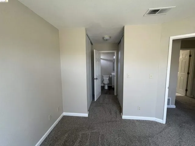 Interior room featuring neutral wall paint, grey patterned carpeting, white baseboards, and white ceiling trim