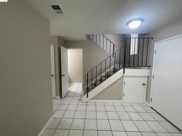 Entryway featuring light-toned tile flooring, a carpeted staircase with black metal railings, a white interior door, and a built-in storage area beneath the stairs