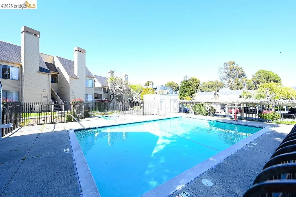 Outdoor swimming pool with concrete decking, surrounded by a metal fence