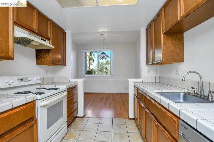 Galley kitchen featuring light wood cabinetry, white tile countertops with matching backsplash, and tile flooring