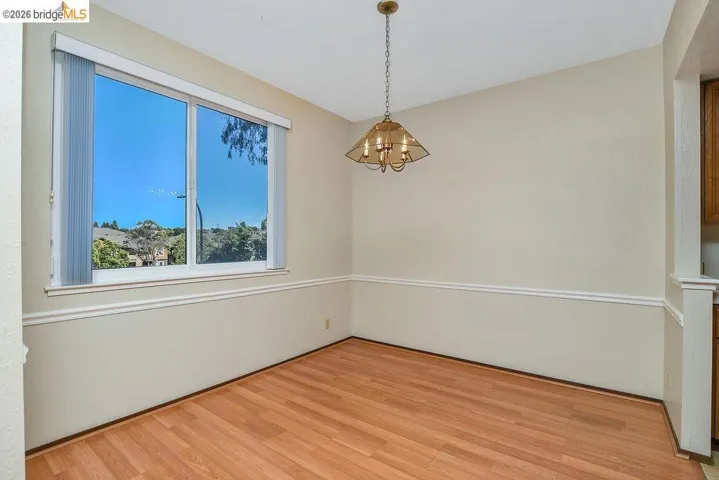 Wood-finish flooring enhances this room, featuring chair rail molding, a large window, and an overhead chandelier with amber-tinted glass shades