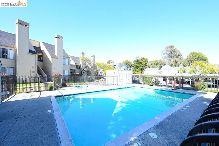 Outdoor swimming pool with concrete decking, surrounded by a metal fence