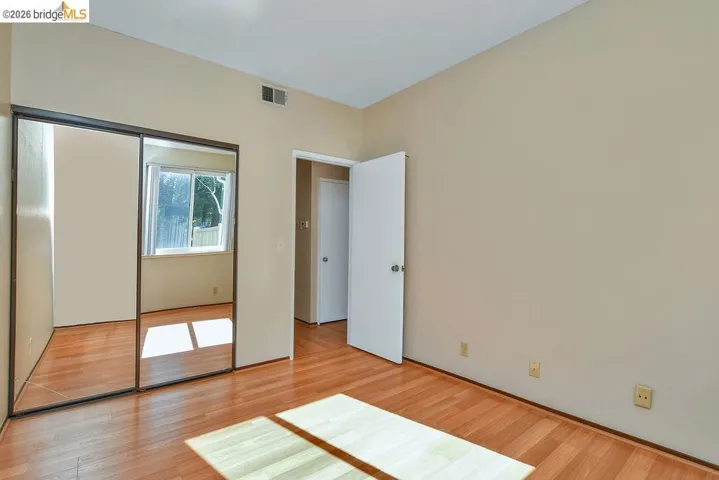 Wood-finish flooring throughout, featuring a mirrored sliding closet door and a window with natural light
