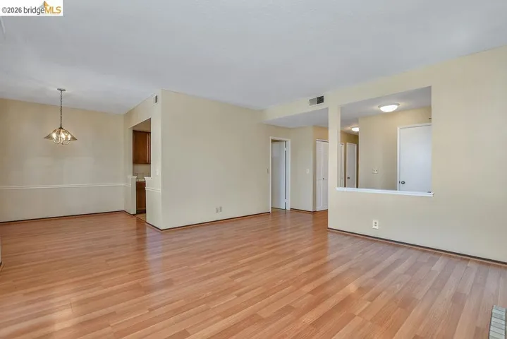 Spacious room featuring wood-finish flooring, neutral-toned walls, and a recessed ceiling with a hanging light fixture