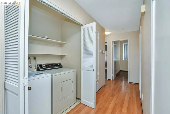 Laundry closet with bi-fold louvered doors, stacked shelving, and wood-finish flooring extending into the hallway