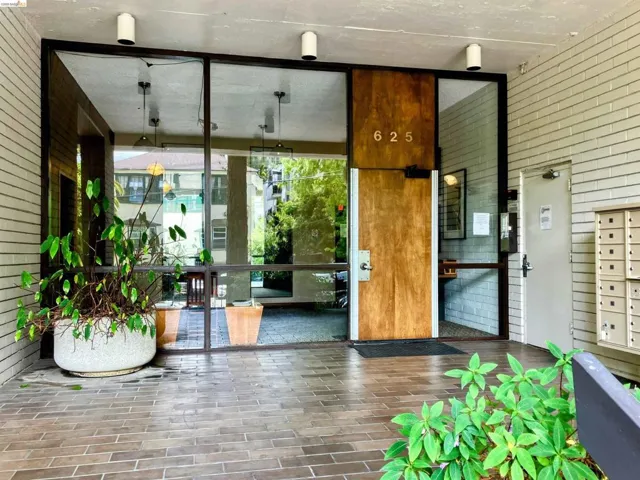 Building entrance featuring a wood-finish door with address numbering, extensive glass paneling, and an overhead lighting array