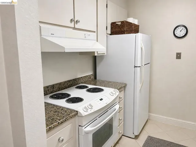 Kitchen area featuring white cabinetry with clear knob hardware, a built-in white range hood, a white electric range, and granite-finish countertops