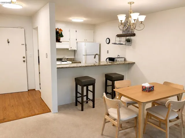 Open-concept living space featuring a breakfast bar with granite-look countertops, white cabinetry, integrated dining area, and wood-finish flooring at the entry