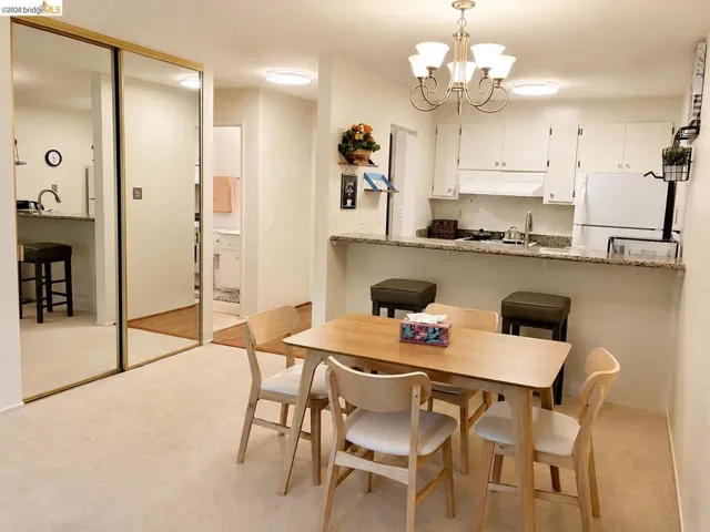 Dining area with neutral carpet flooring and a kitchen featuring white cabinetry, a stone-finish countertop, and a breakfast bar