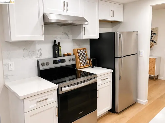 Modern kitchen featuring white shaker cabinetry, stainless steel appliances, white quartz countertops, and a full-height marble-look backsplash