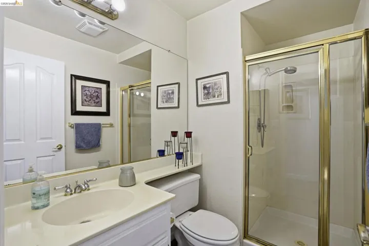 Bathroom featuring a glass-enclosed shower with gold-tone framing, a vanity with an integrated sink and light-toned countertop, a full-width mirror, and overhead vanity lighting