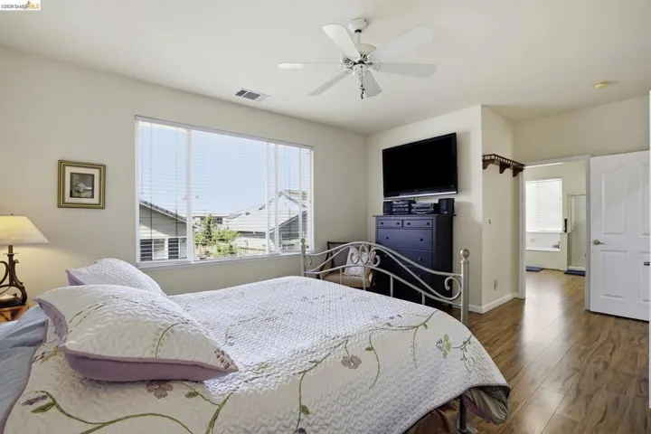 Spacious room featuring wood-finish flooring, a large window with blinds, and a ceiling fan