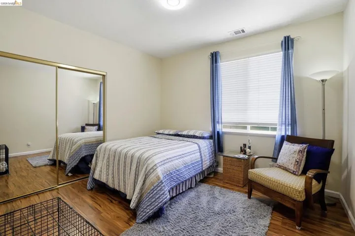 Bedroom featuring wood-finish flooring, a window with blinds, and mirrored sliding closet doors