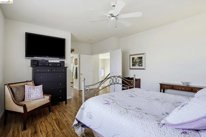 Spacious room featuring wood-finish flooring, a ceiling fan, and white walls