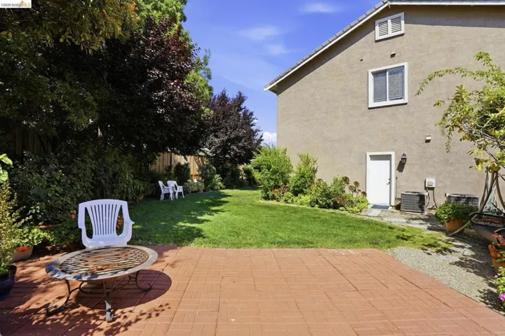 Expansive backyard featuring a red paver patio, a lush green lawn, mature trees, and established shrubbery