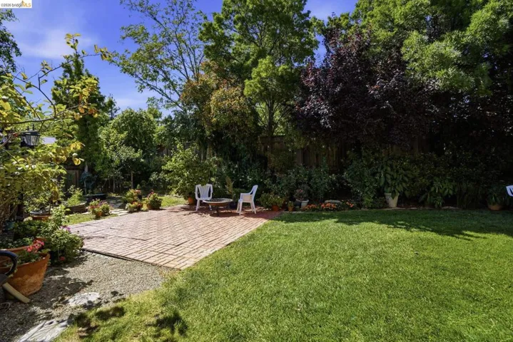 Expansive backyard featuring a manicured lawn, brick paver patio, gravel border, and mature trees