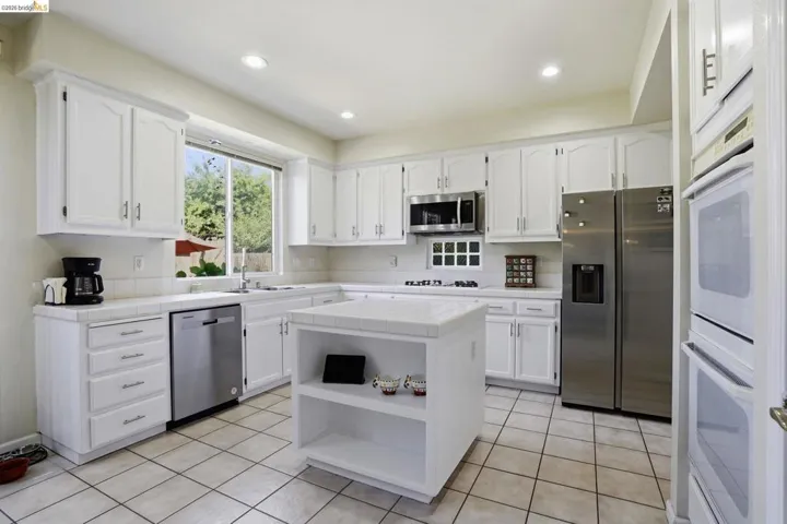 Kitchen featuring a central island with open shelving, white cabinetry, stainless steel appliances, a tile backsplash, and recessed lighting
