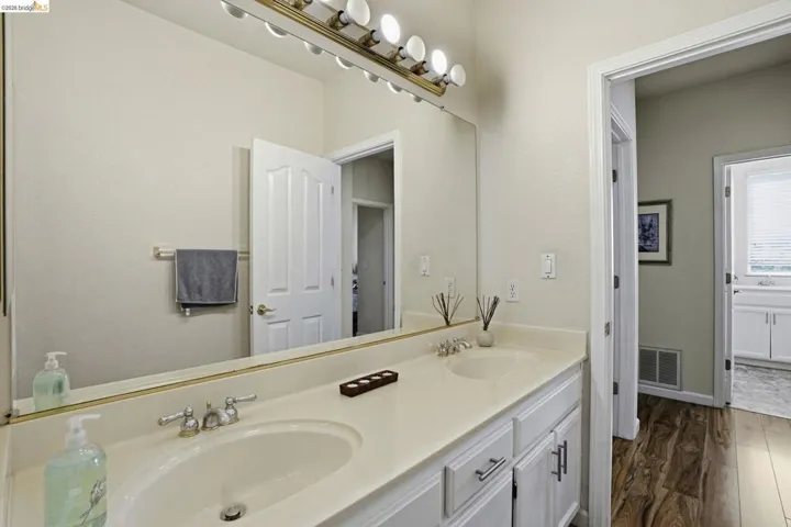 Dual vanity with integrated sinks, white cabinetry, chrome hardware, and a full-width mirror with overhead lighting