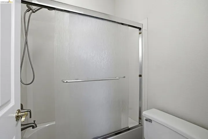 Bathtub with brushed nickel fixtures, a handheld showerhead, and a frosted glass sliding door