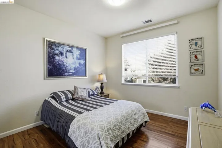 Spacious room featuring wood-finish flooring, a large window with blinds, and a built-in air vent