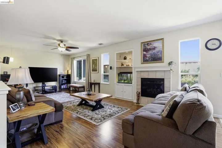 Living room featuring wood-finish flooring, a ceiling fan, and multiple windows
