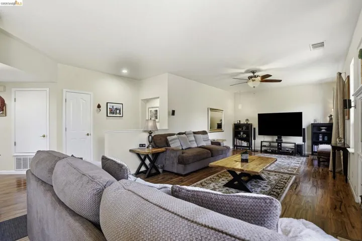 Open-concept living area featuring wood-finish flooring, a ceiling fan with integrated lighting, and neutral wall tones