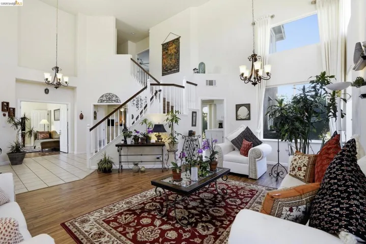 Voluminous living area featuring high ceilings, wood-finish flooring, and a grand staircase with white risers and dark wood handrails