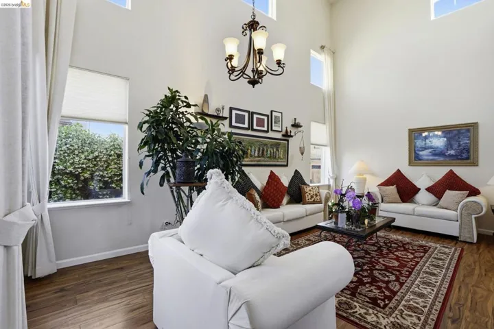 Expansive room featuring high ceilings, upper transom windows, wood-finish flooring, a decorative chandelier, and perimeter wall art