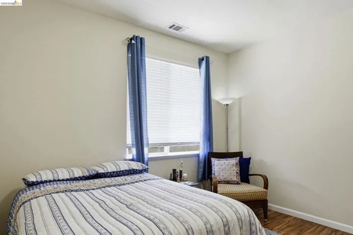 Bedroom featuring light-toned walls, wood-finish flooring, a window with blinds, and white baseboards