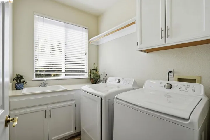 Dedicated laundry space featuring a utility sink, white cabinetry with silver hardware, and a window with horizontal blinds