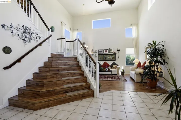 Two-story foyer featuring a wood-finish staircase with white balusters, ceramic tile flooring, and high ceilings