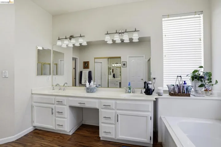 Dual vanity with ample counter space, integrated sinks, white cabinetry, and wood-finish flooring