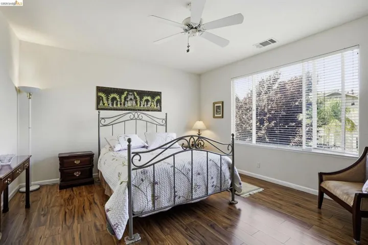 Spacious room featuring wood-finish flooring, a large window with blinds, and a ceiling fan